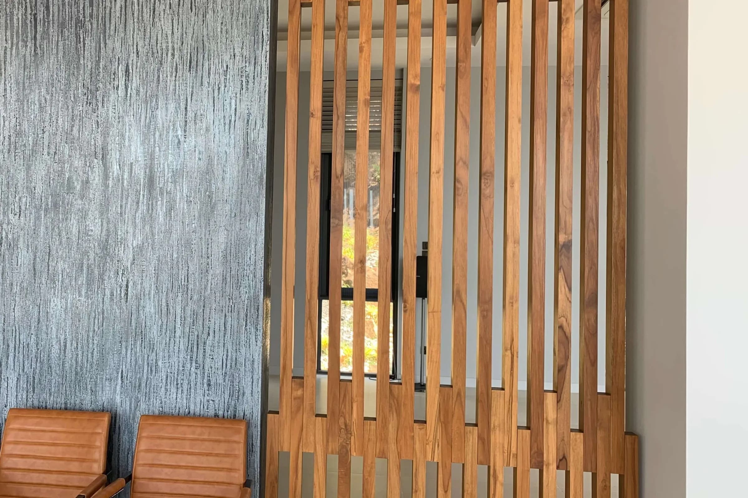 Slatted teak screen beside a textured feature wall, with leather chairs in a finished interior
