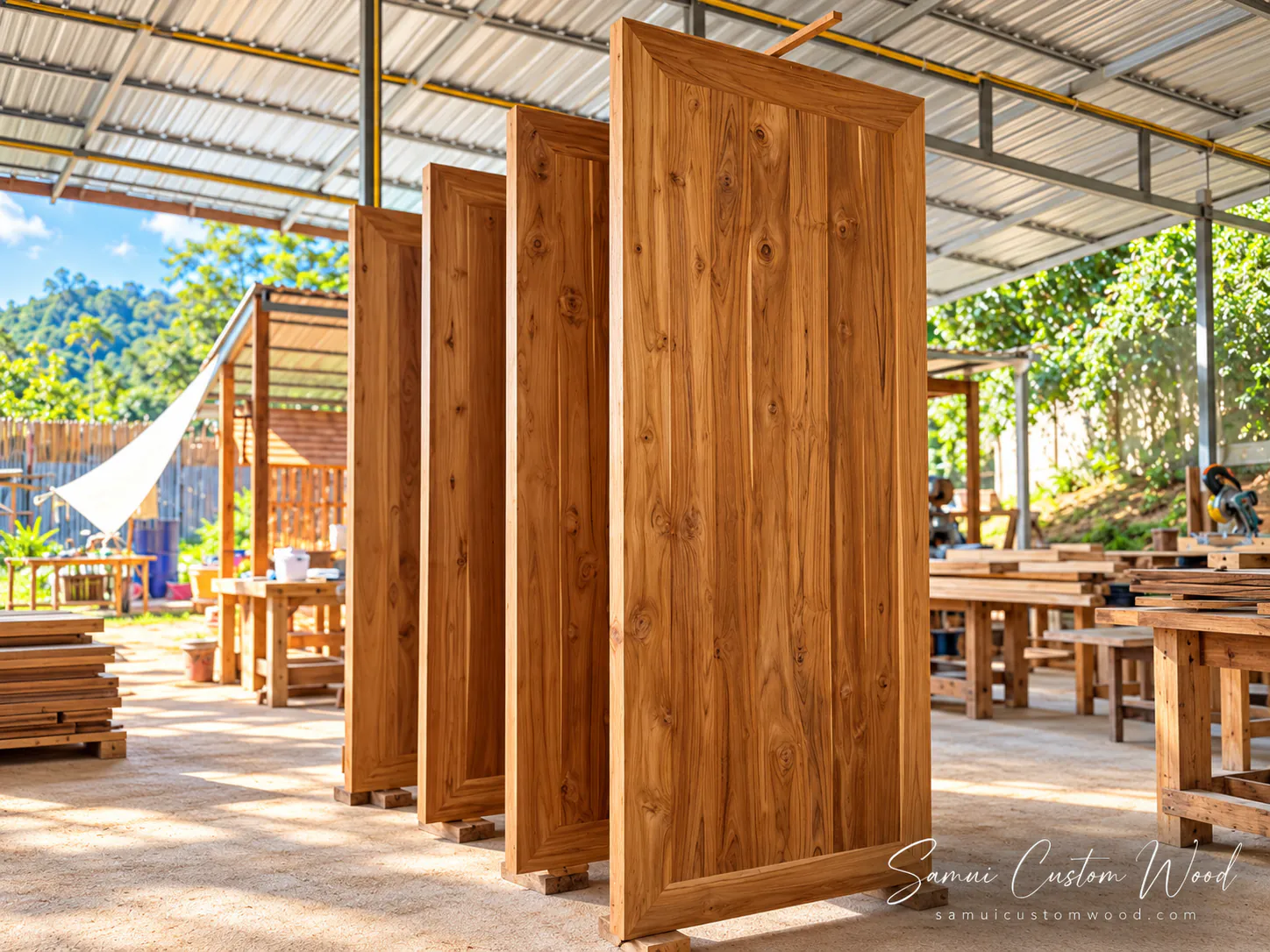 Four solid teak door leaves standing upright on blocks in the workshop
